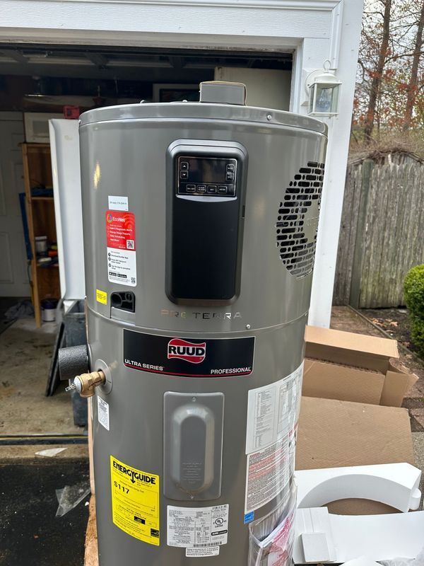 A new electric water heater, gray with black digital display, sits outside a garage.