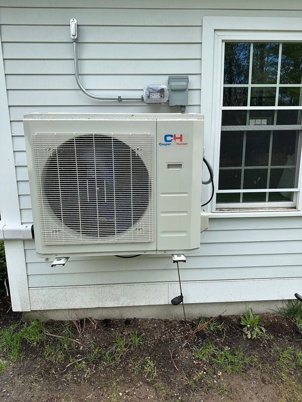 White wall-mounted air conditioner unit next to a window on the side of a white building.