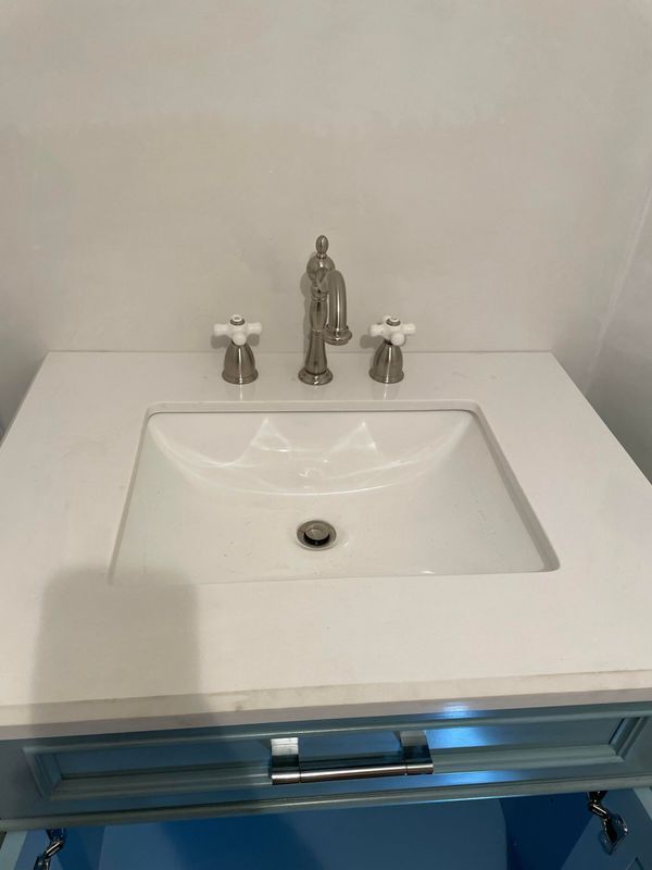 White bathroom sink with silver faucet and knobs, set in a white countertop above a blue cabinet.