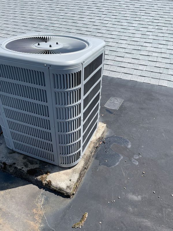 Gray air conditioning unit on a dark roof with a gray background.