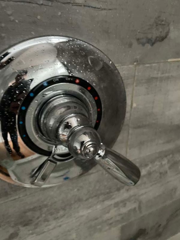 Chrome shower valve with temperature indicator, on gray tiled wall.