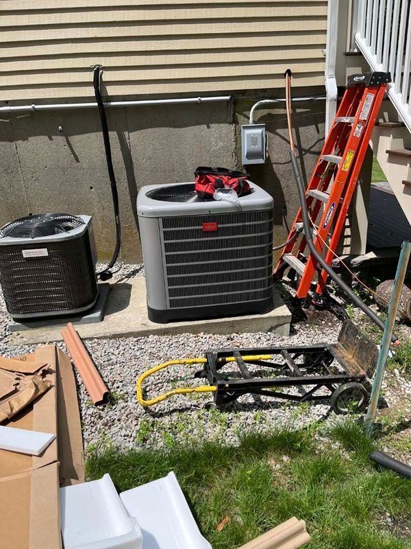 Air conditioning units next to a building, with a ladder and dolly nearby.