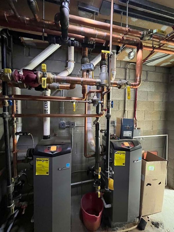 Two gray water heaters with copper pipes in a basement setting.
