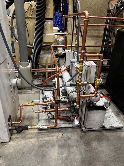 Copper pipes and fittings connected to machinery, likely part of an industrial system, indoors.