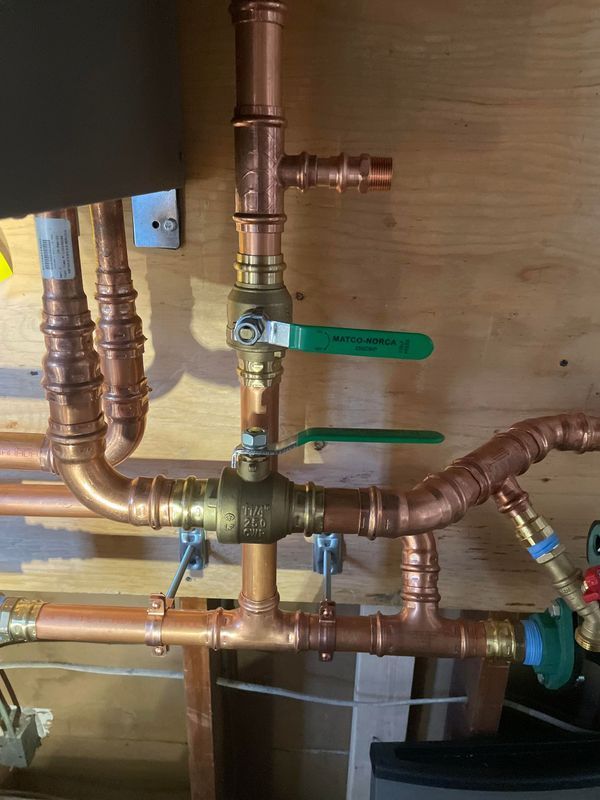 Copper pipes and valves against a wooden wall; two green-handled ball valves are prominent.