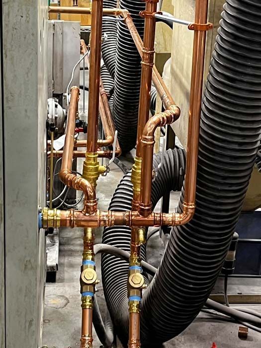 Copper pipes, fittings, and valves installed around a large gray industrial machine.