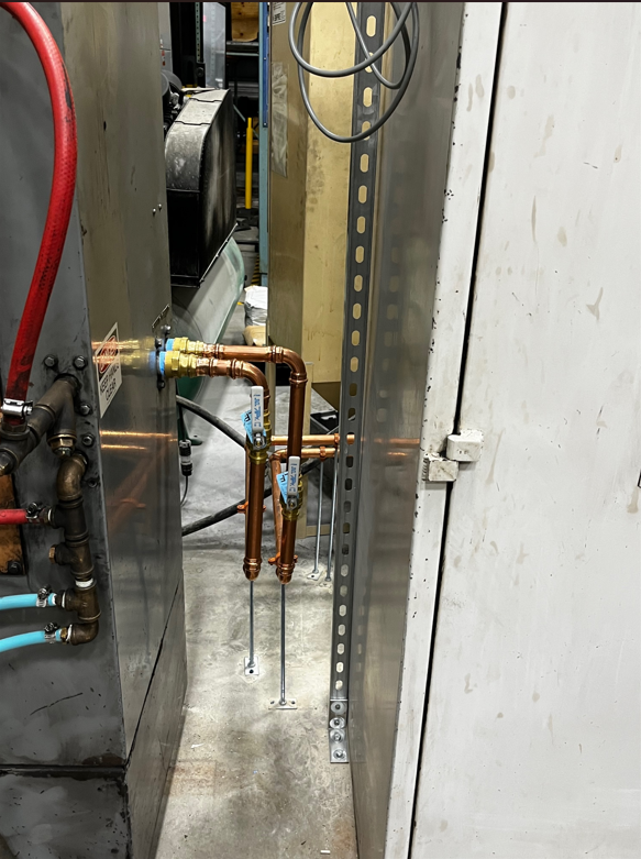 Copper pipes and fittings in industrial setting; gray metal cabinets, metallic conduit.