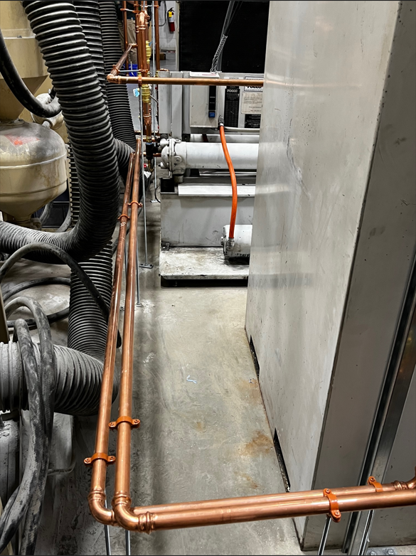 Copper pipes installed in an industrial setting, attached to machinery and the floor.