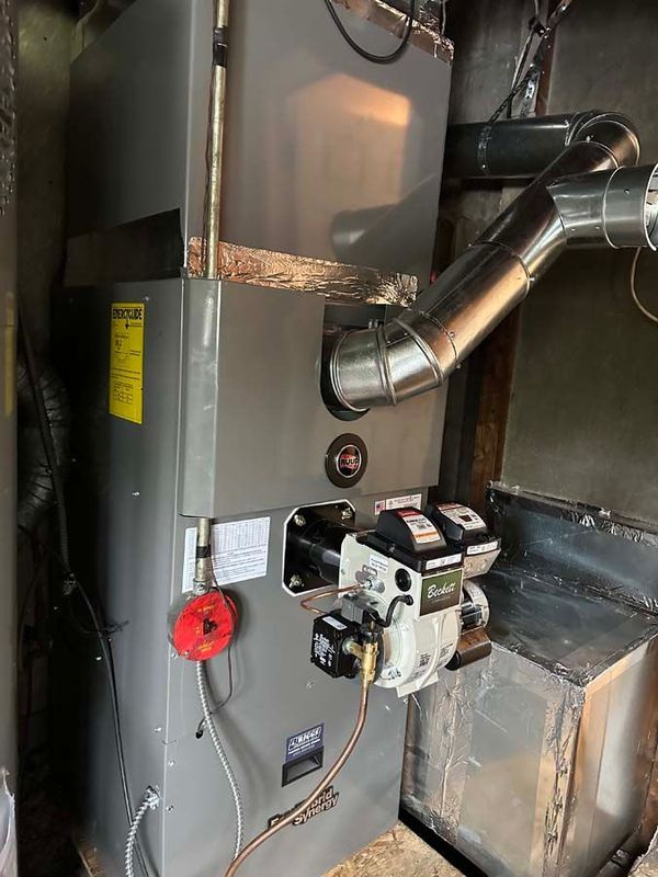 Oil furnace with burner and flue pipe in a utility room.