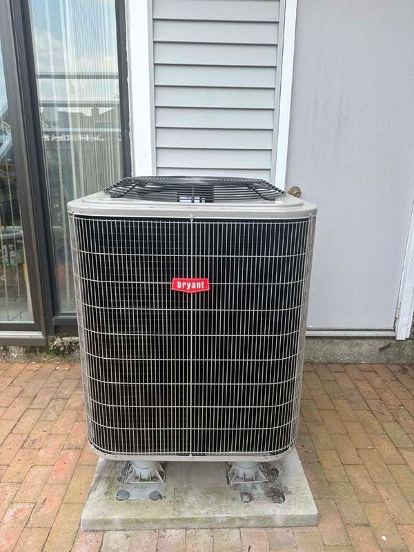 Bryant air conditioning unit on a concrete pad, against a gray wall and brick patio.