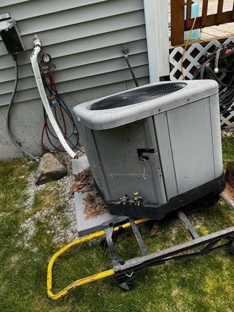 Outdoor air conditioning unit tilted on a dolly near a house.