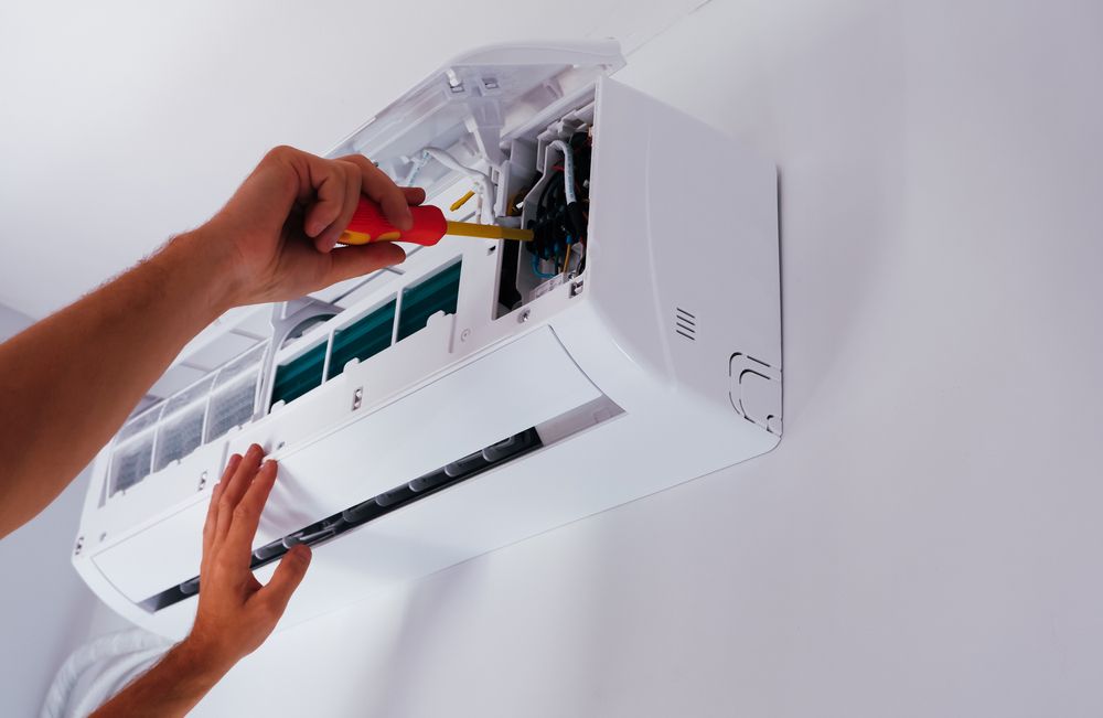 Person using a screwdriver to repair a white wall-mounted air conditioning unit.
