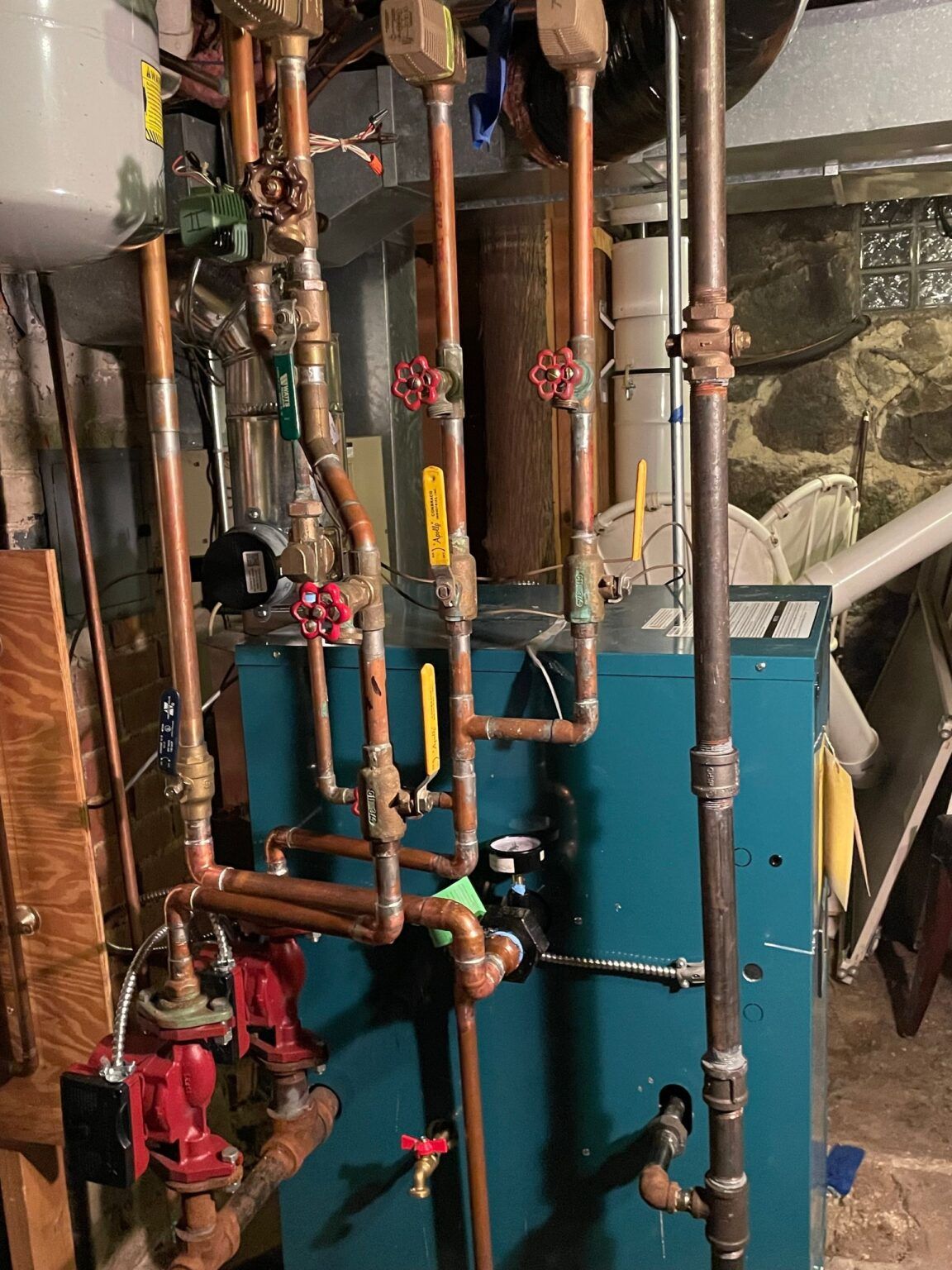 Blue boiler with copper pipes, valves, and a red pump in a basement setting.