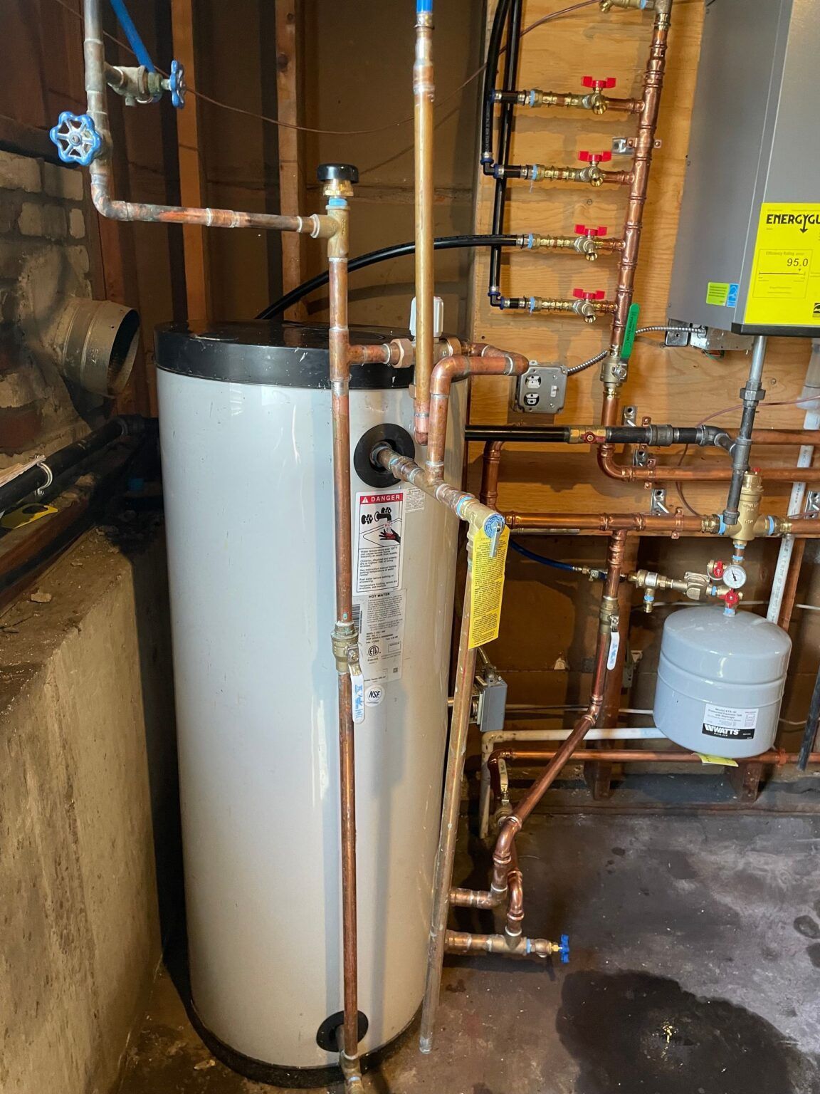 White water heater with copper pipes in a basement.