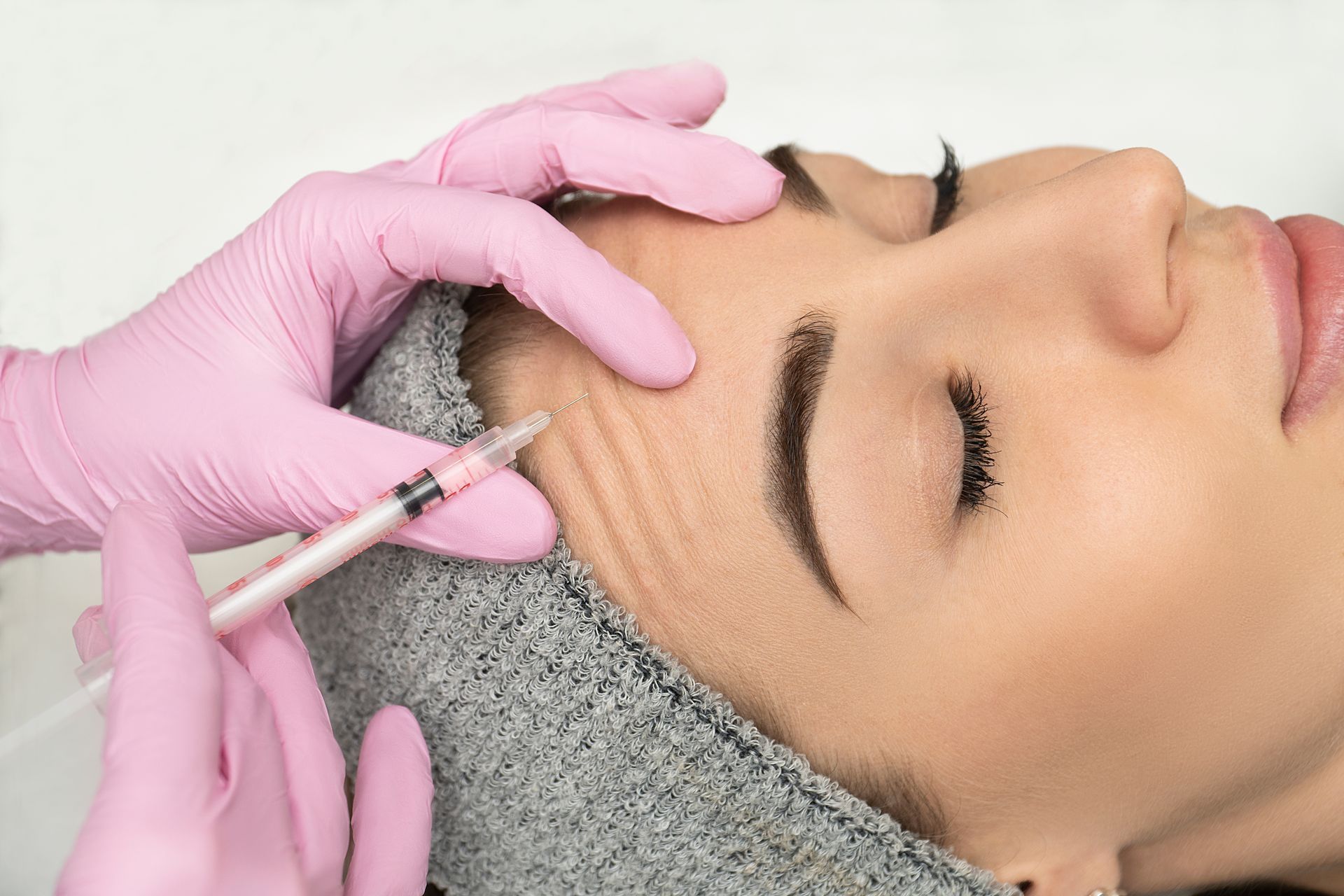 A woman is getting a botox injection in her forehead.