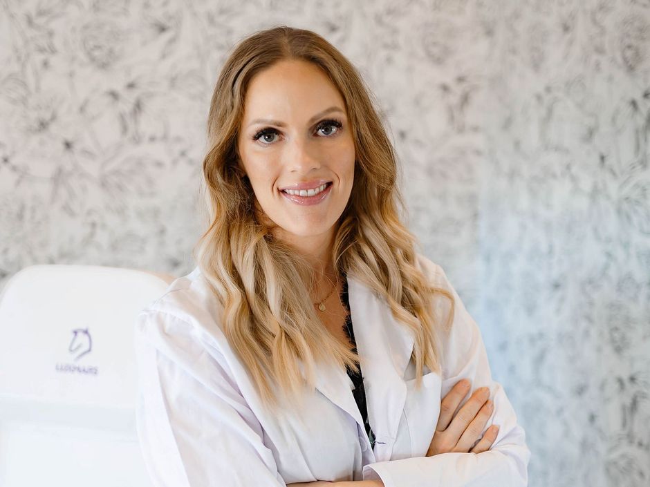 A woman in a white lab coat is standing in front of a table with her arms crossed.