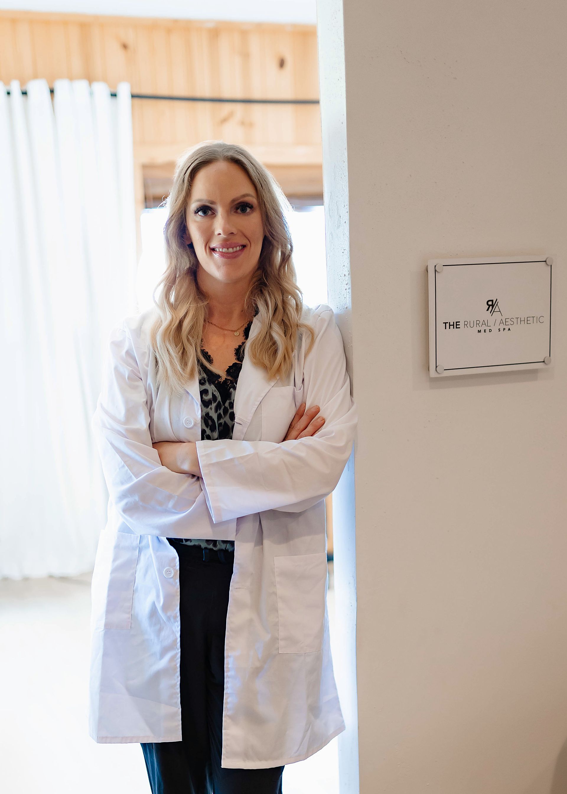 A woman in a lab coat is standing in a doorway with her arms crossed.