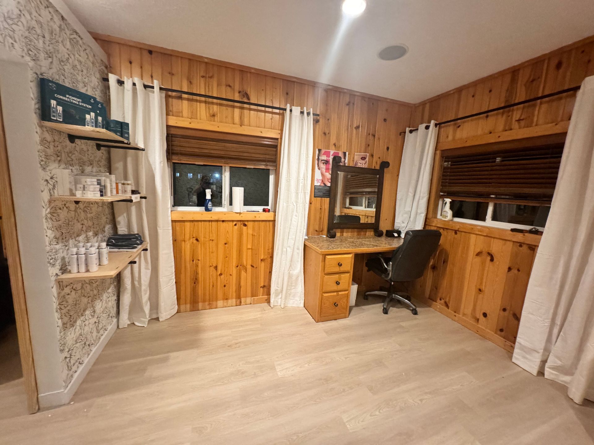 A room with wood paneling , a desk , a chair and a mirror.