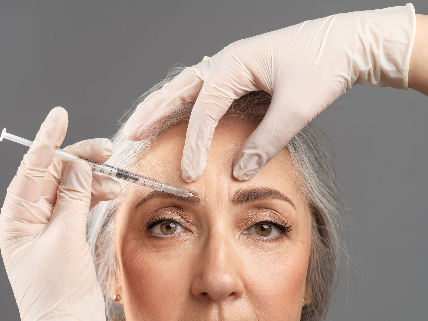 A woman is getting a botox injection in her forehead.