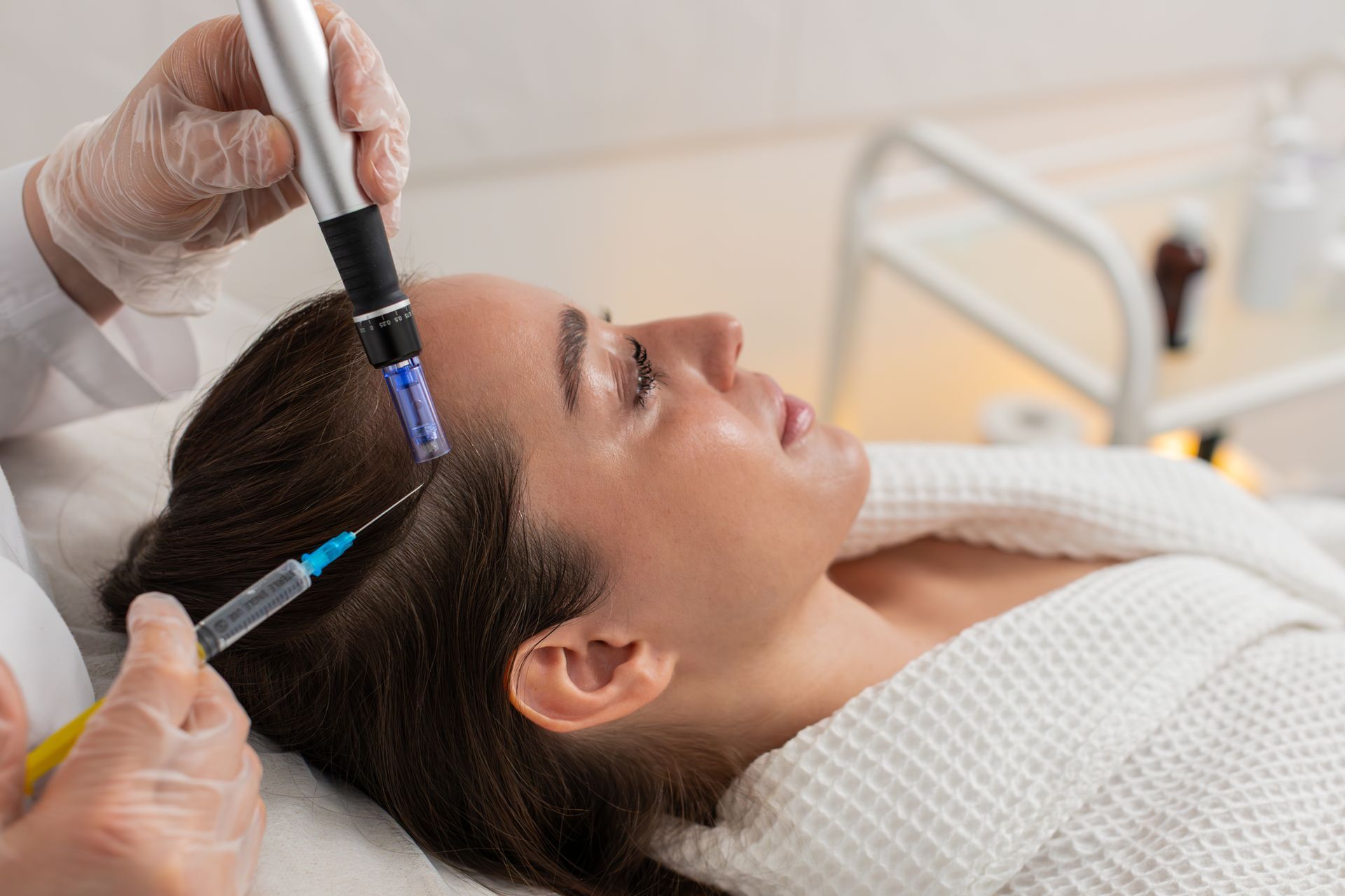Woman receiving microneedling treatment on her scalp; gloved hands, medical setting.