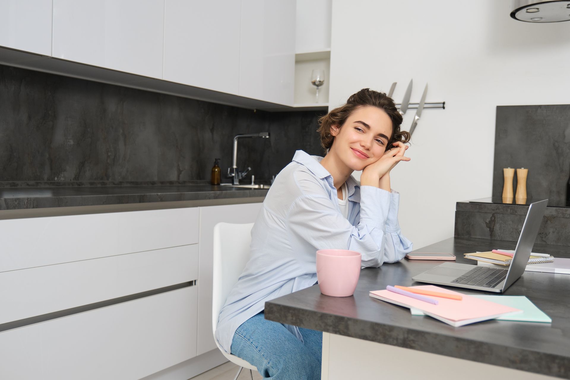 A woman is sitting at a table with a laptop and a cup of coffee.