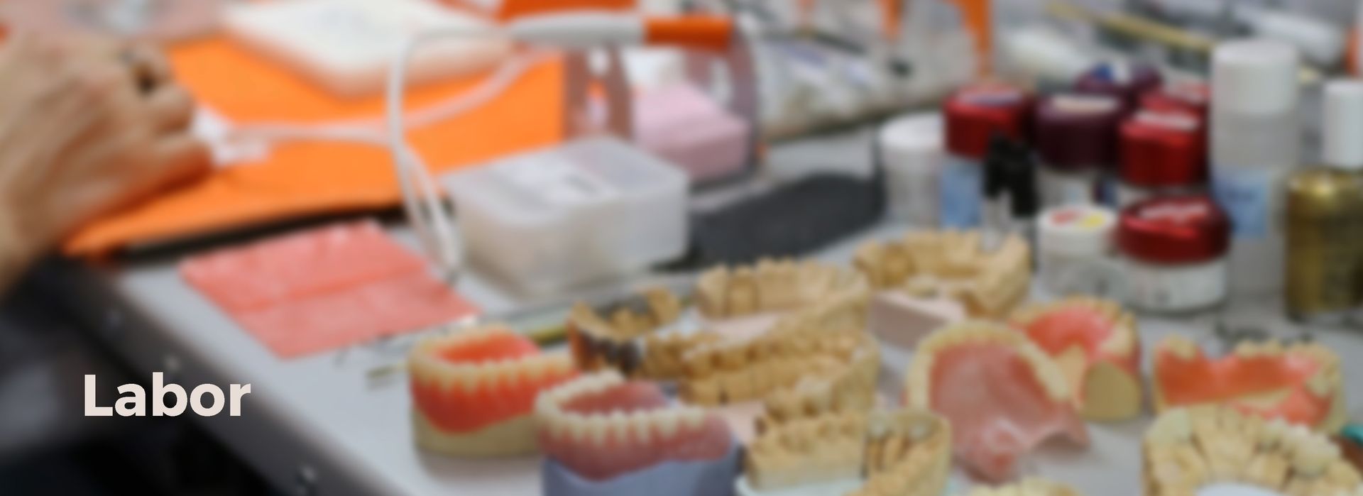 Eine Person sitzt an einem Tisch, auf dem ein Stapel Zahnprothesen liegt.