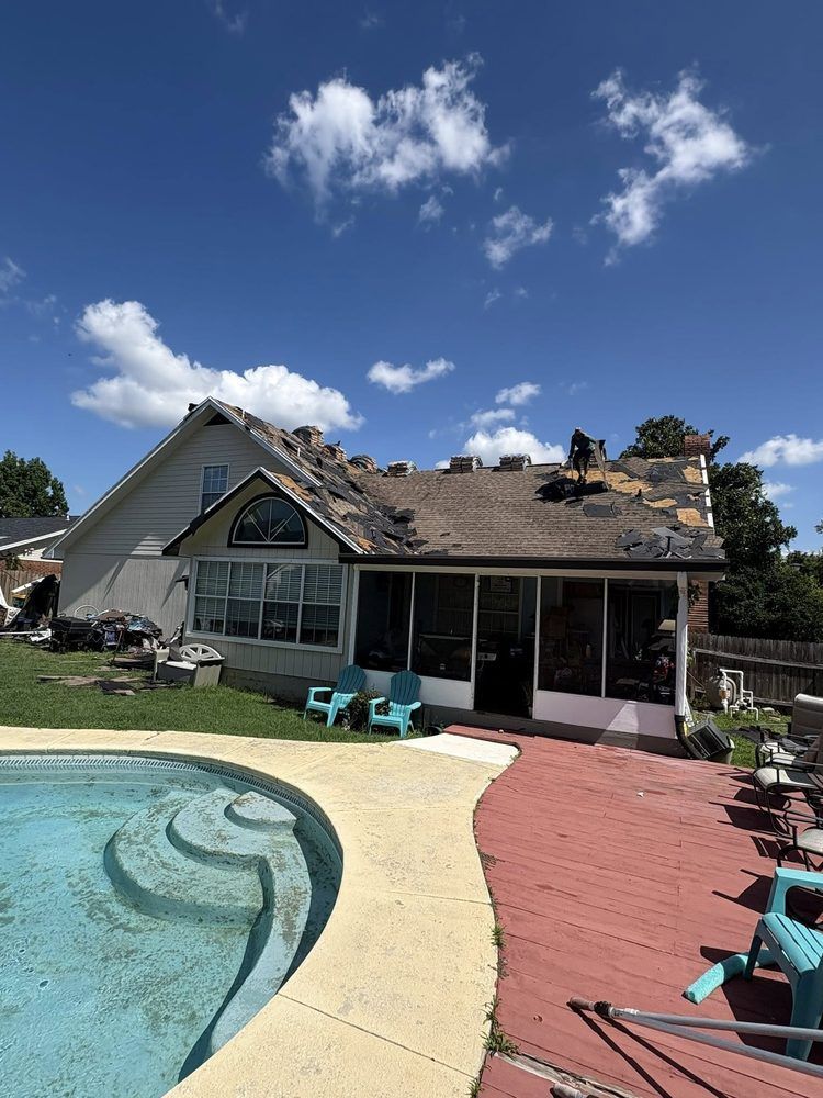 House with partially removed roof, worker on roof. Backyard with pool and red deck. Sunny day.