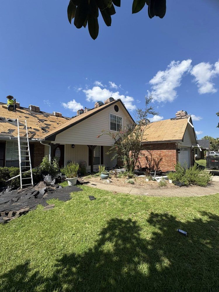 Roofing work on a house; workers on the roof, ladder, blue sky, and lawn.