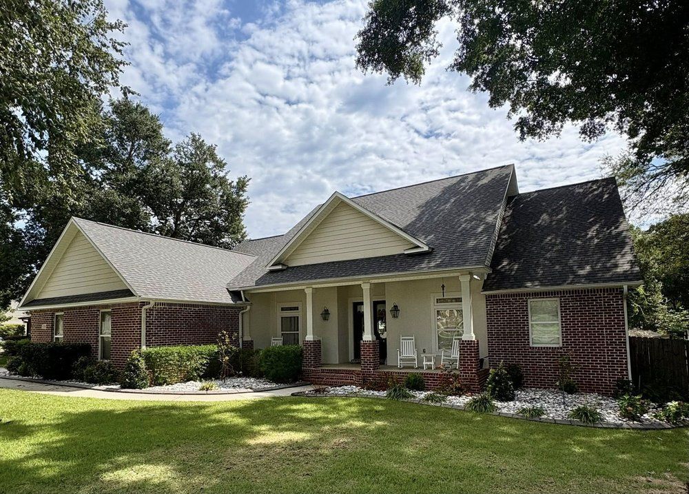 A single-story house with a dark roof, brick siding, and green grass.