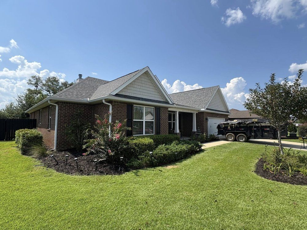 Brick house with dark roof, lush green lawn, and blue sky.