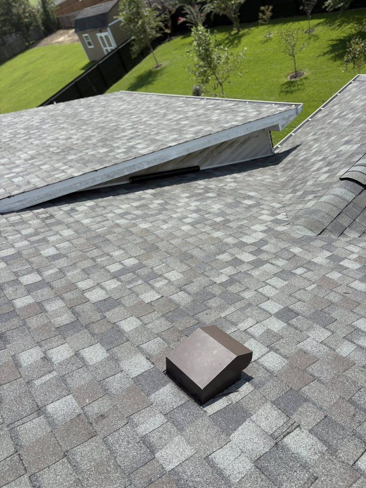 Overhead view of a gray shingled roof with an angled vent and a brown, square vent, set outdoors.