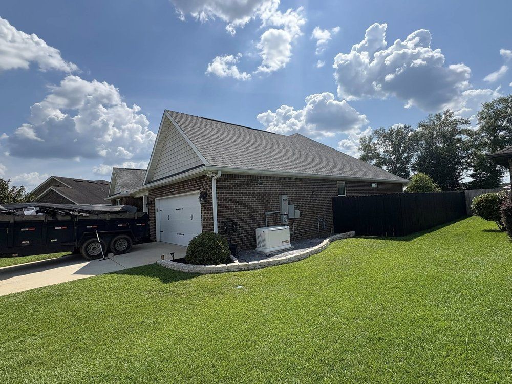 Garage with gray roof, white door, brick and siding exterior, and green lawn under a cloudy sky.