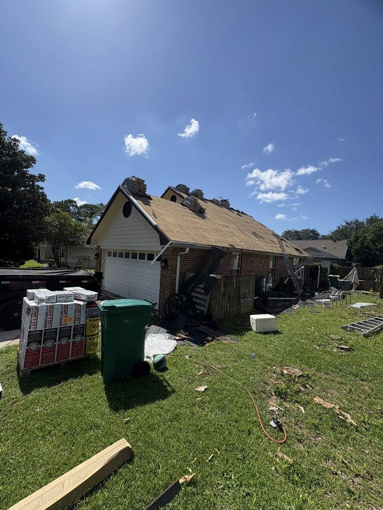 Garage under construction, roof partially removed, materials and trash strewn about a grassy yard under a sunny sky.