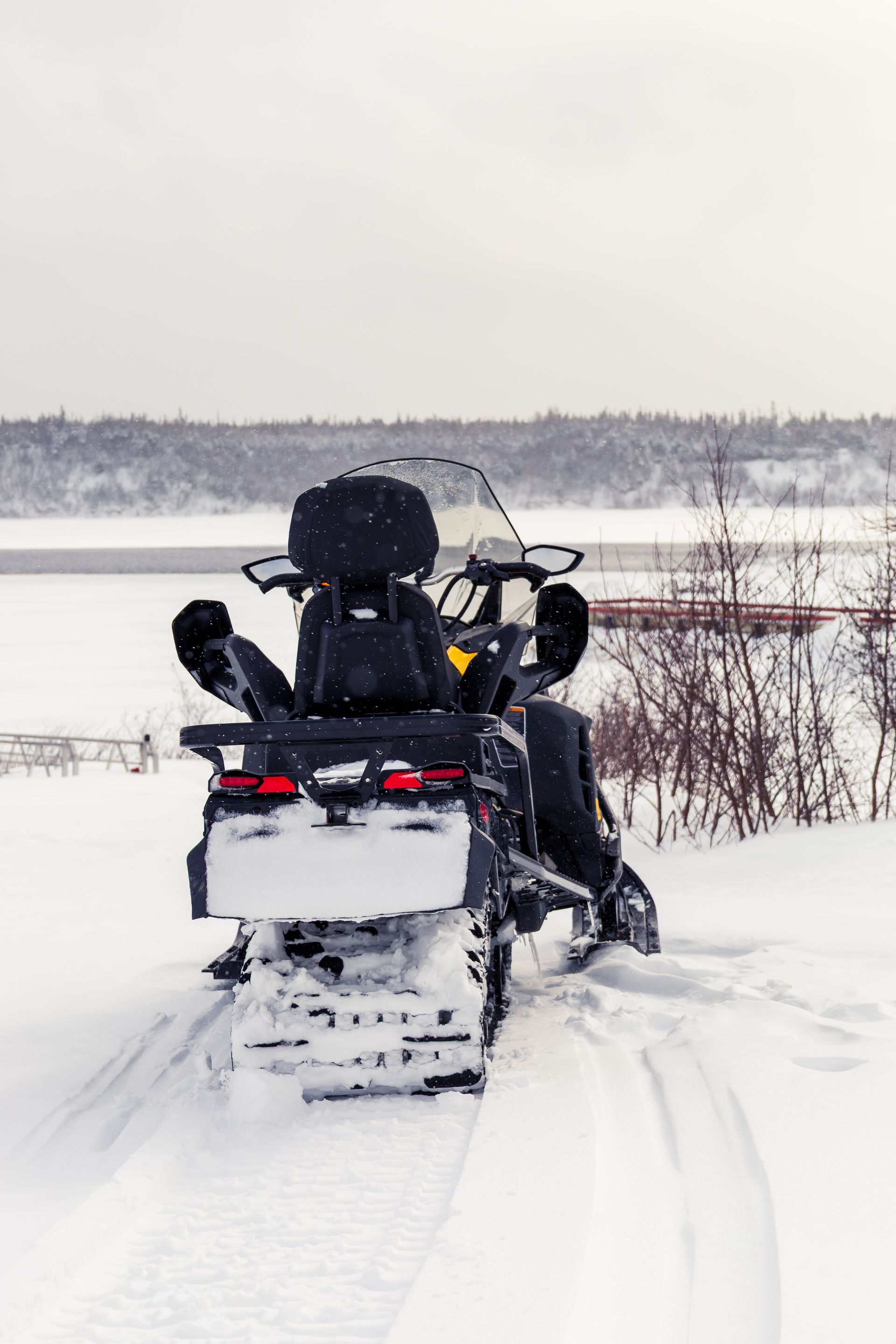 Snowmobile on a snowy trail beside a frozen lake, with gear strapped on the back.