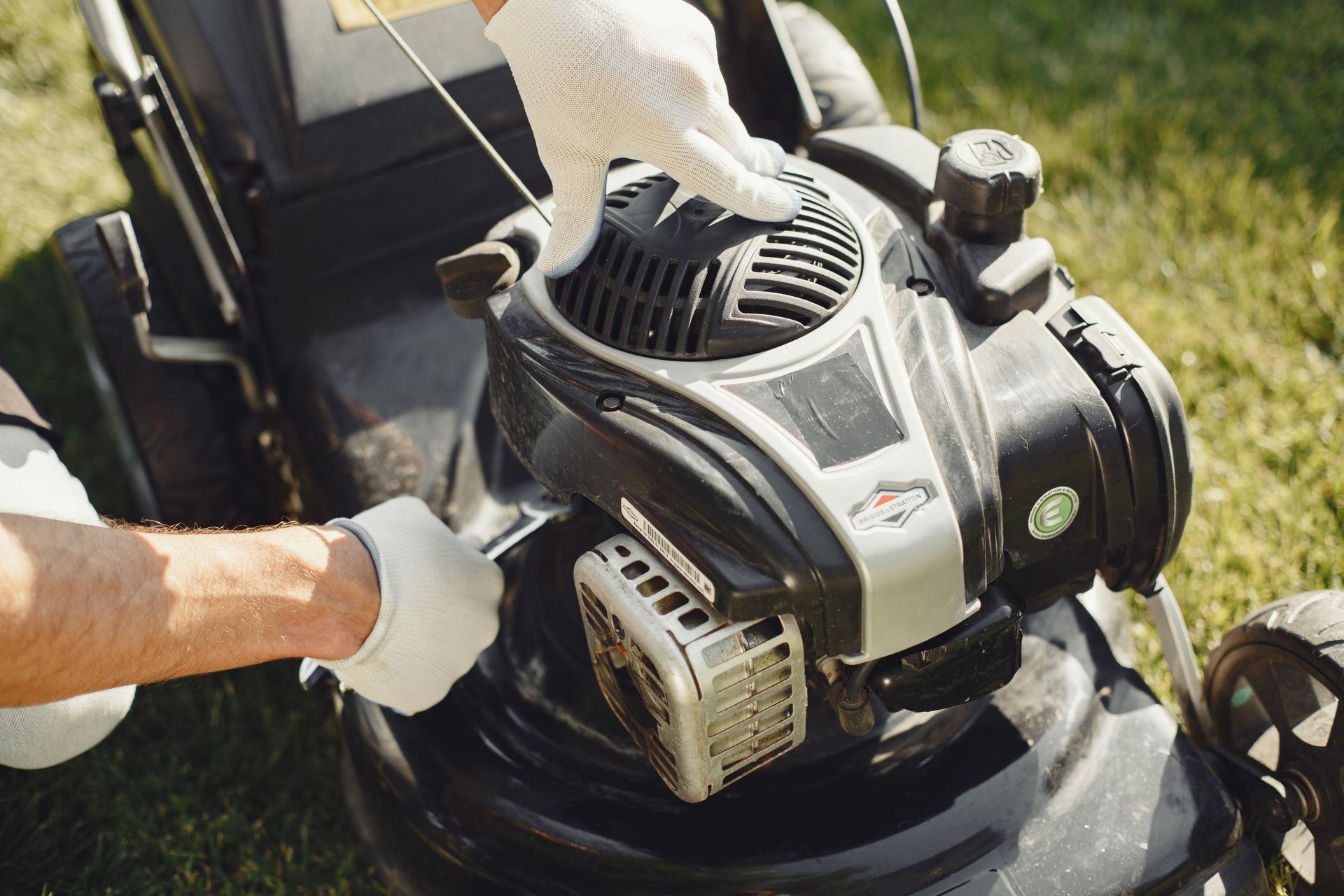 Person pushing a gas lawn mower on grass, close-up of the engine and handle.
