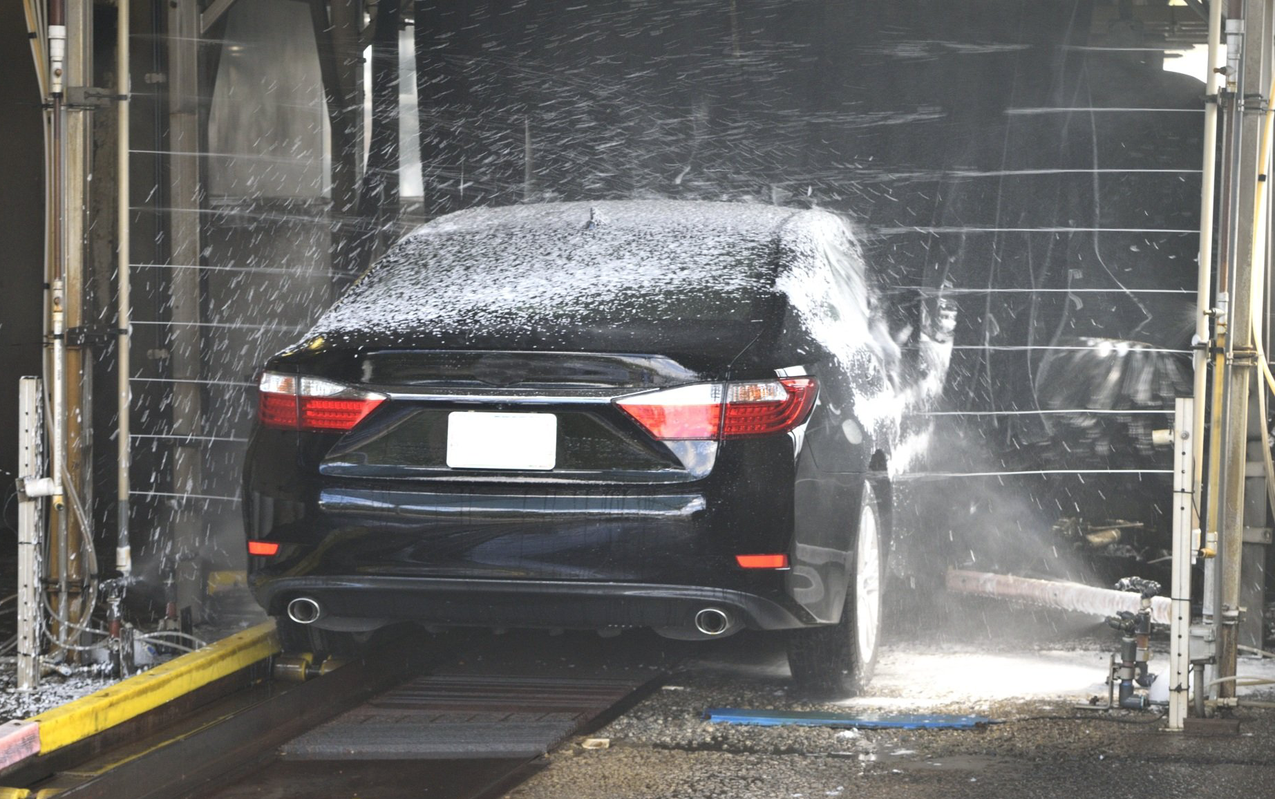 Black car in a carwash, covered in foam and water, inside a bay.