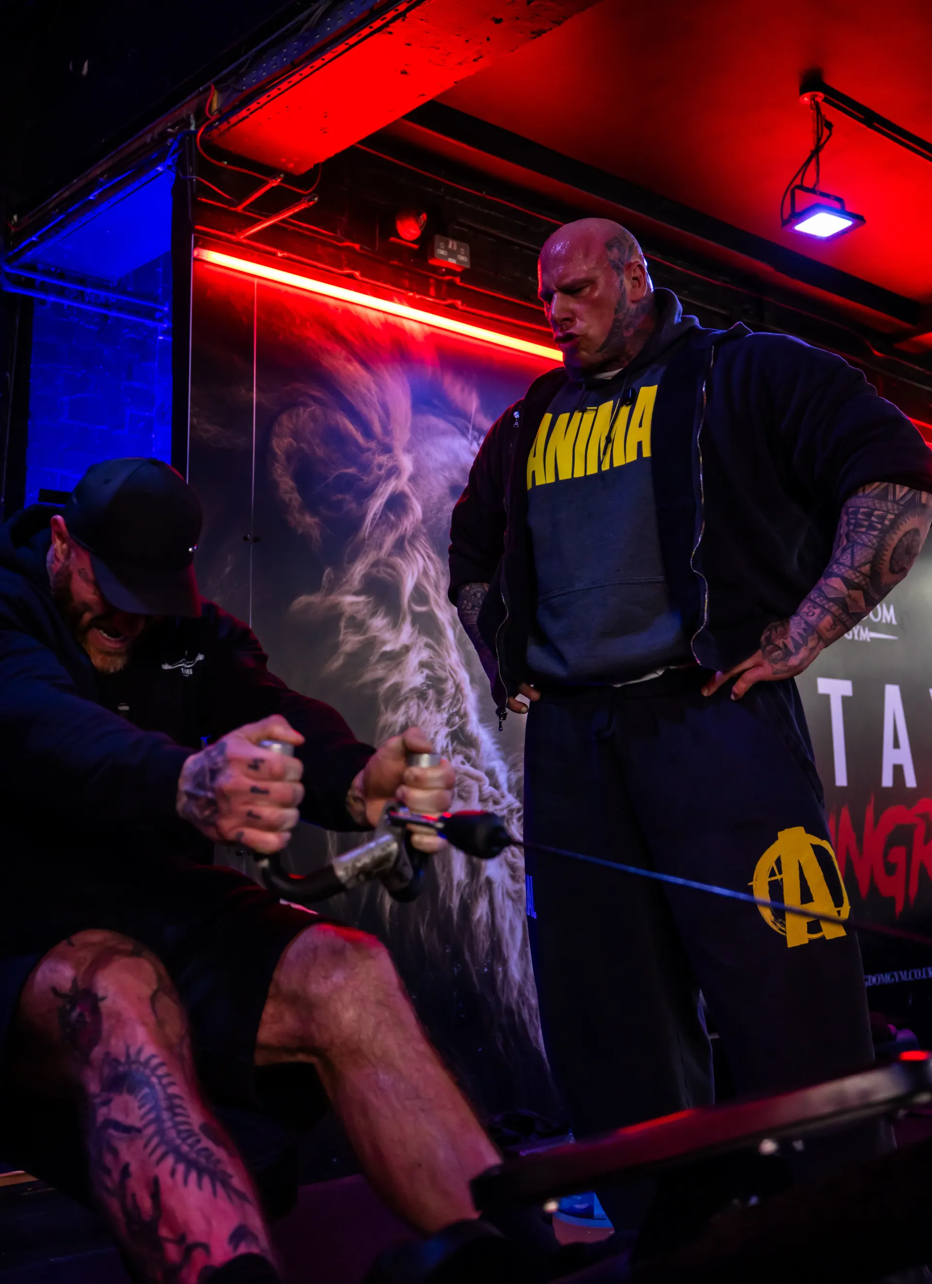 A muscular man in a black shirt and shorts, fist clenched, looks forward.