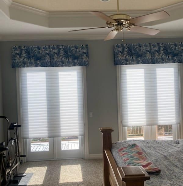 Two windows with white blinds, blue patterned valances, and a ceiling fan.
