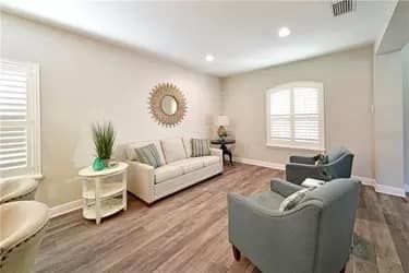 Living room with couch, chairs, wood floor, and sunlight.