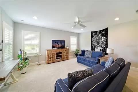 Spacious living room with blue sofas, wooden media console, tapestry, and light-colored walls.