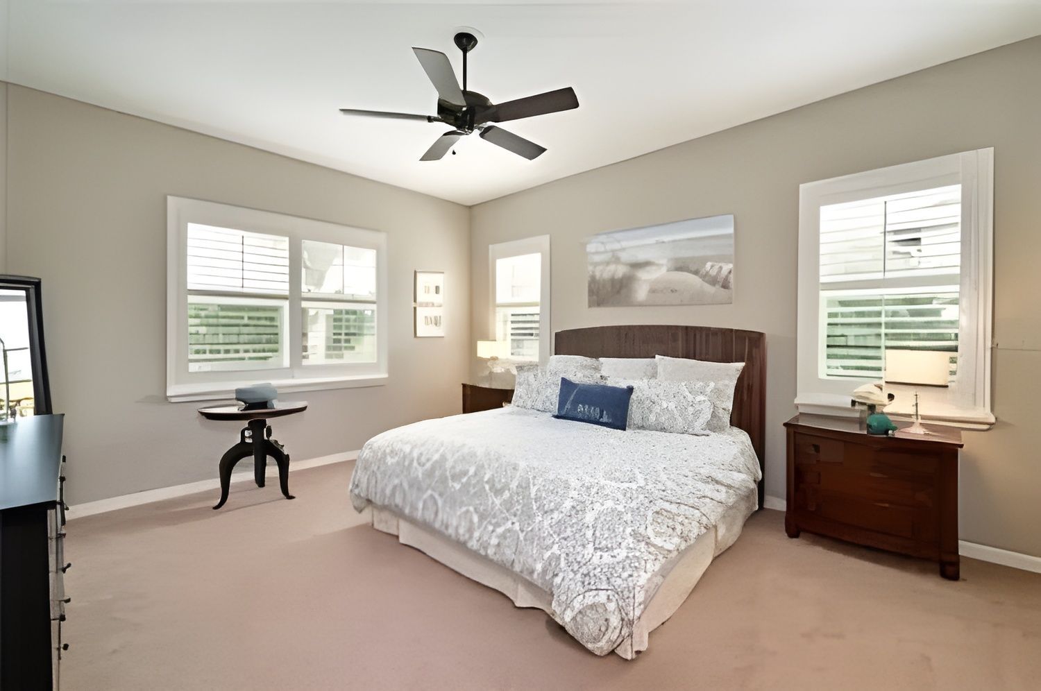 Bedroom with bed, windows, ceiling fan, and wooden furniture. Soft color palette.