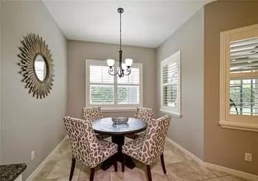 A small dining area with a round table, four chairs, and a chandelier, with neutral-colored walls and a window.