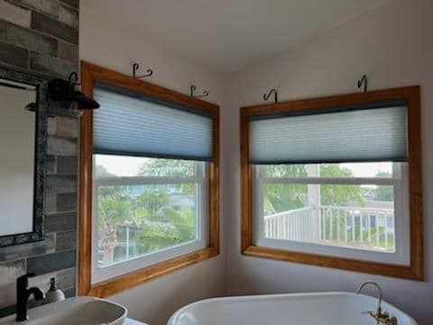 Bathroom corner with windows, light blue shades, and wooden frames. A tub is in front.