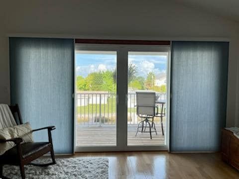 Room with sliding glass doors, blue panel curtains, and a rocking chair. Exterior view of greenery and a deck.
