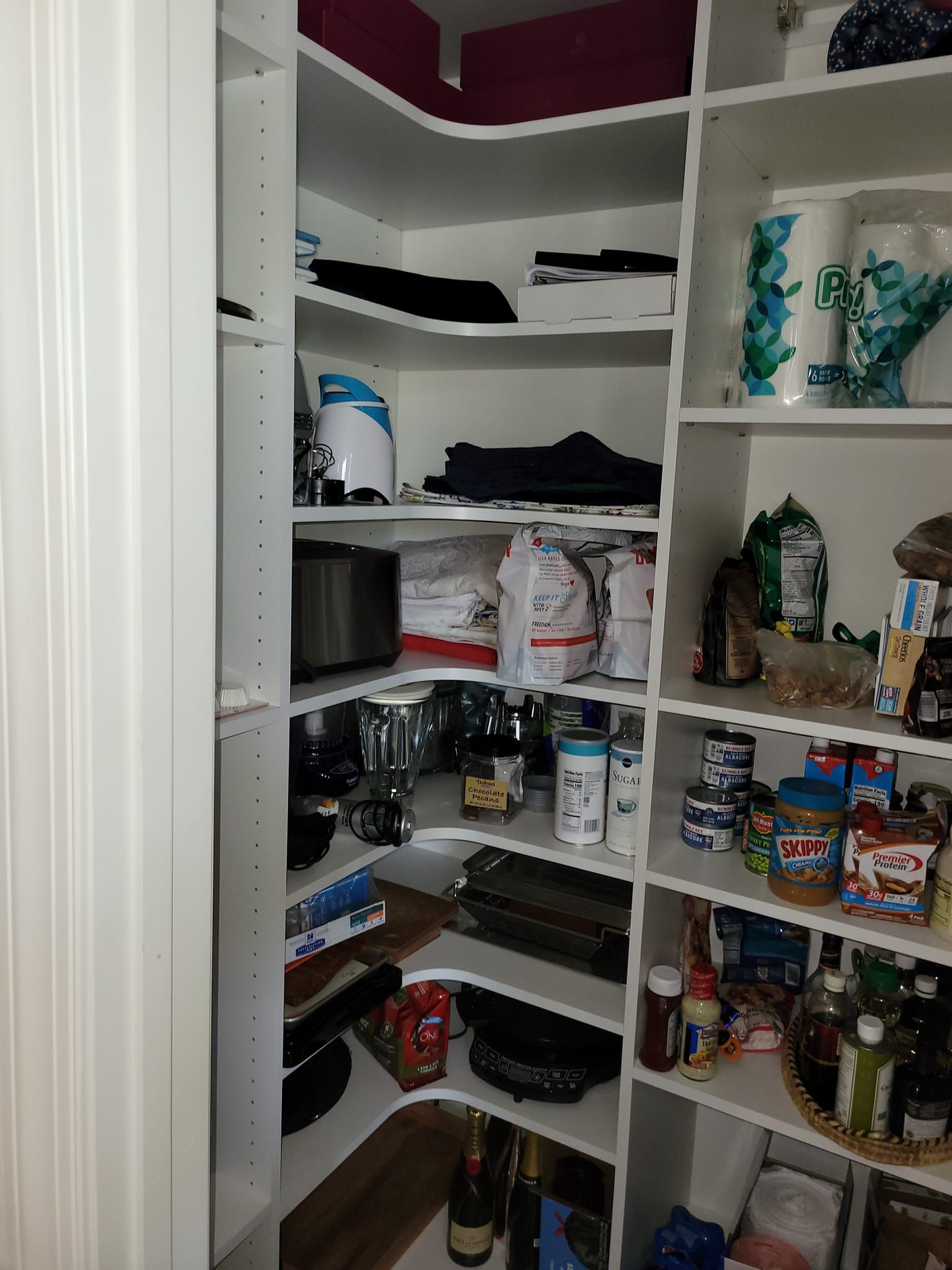 White pantry with curved shelves, stocked with food, appliances, and paper towels.
