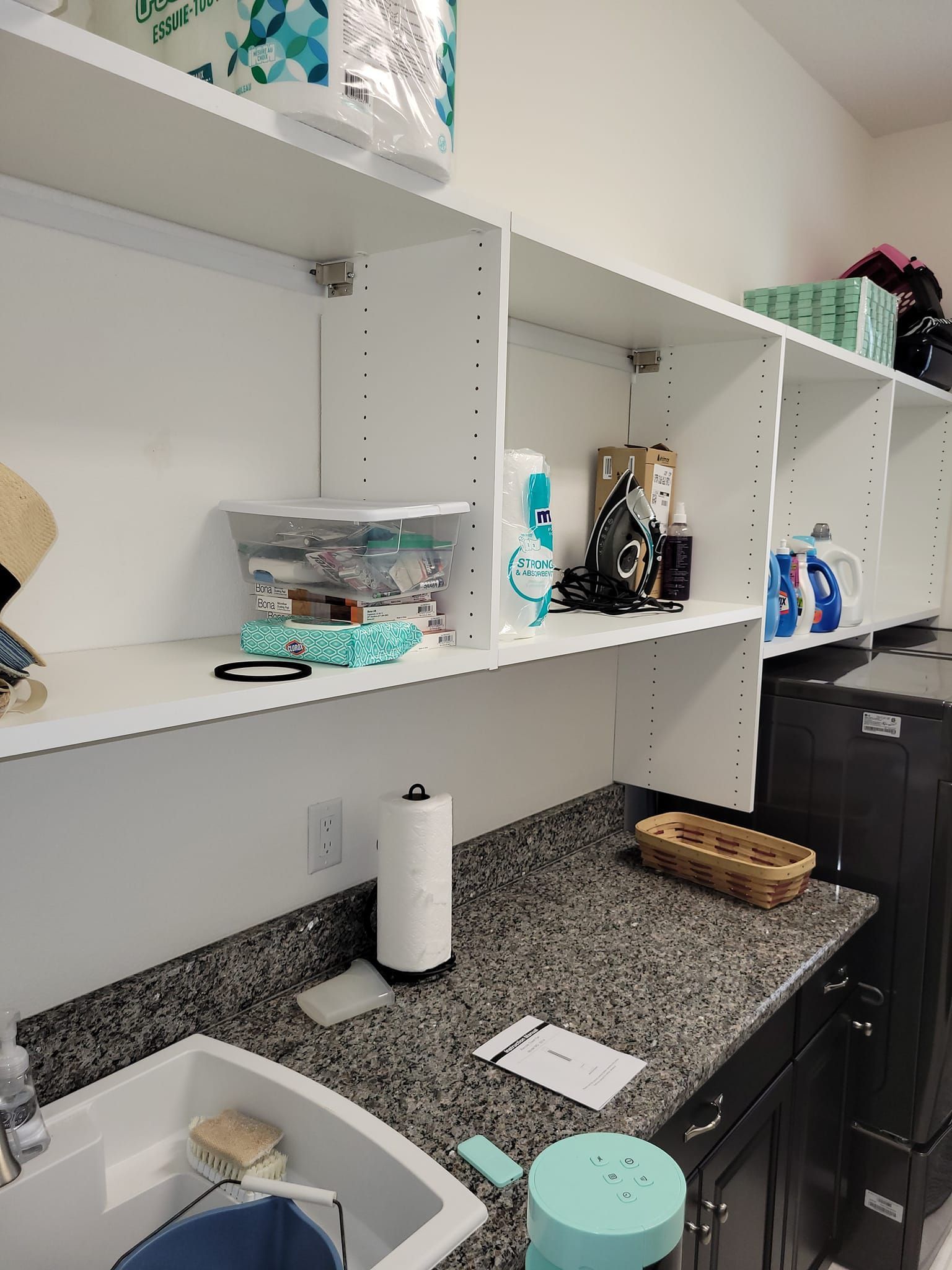 Laundry room with white shelves, countertop, sink, and washer/dryer. Items stored on shelves.