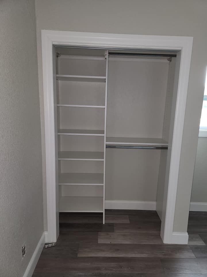 Empty white closet with built-in shelves on the left and a rod for hanging clothes on the right.