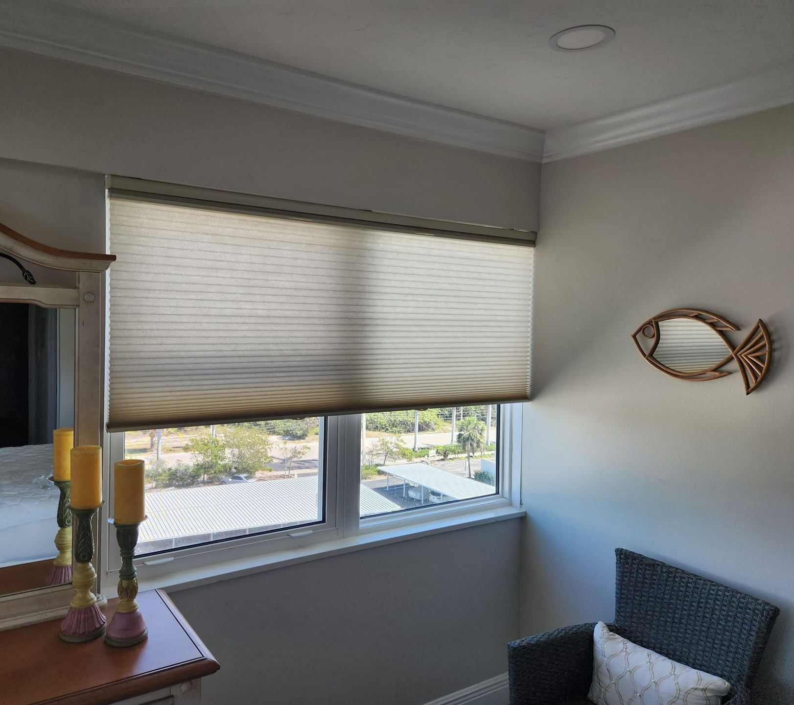 Beige pleated window shade in a room with a window, chair, and fish-shaped mirror.