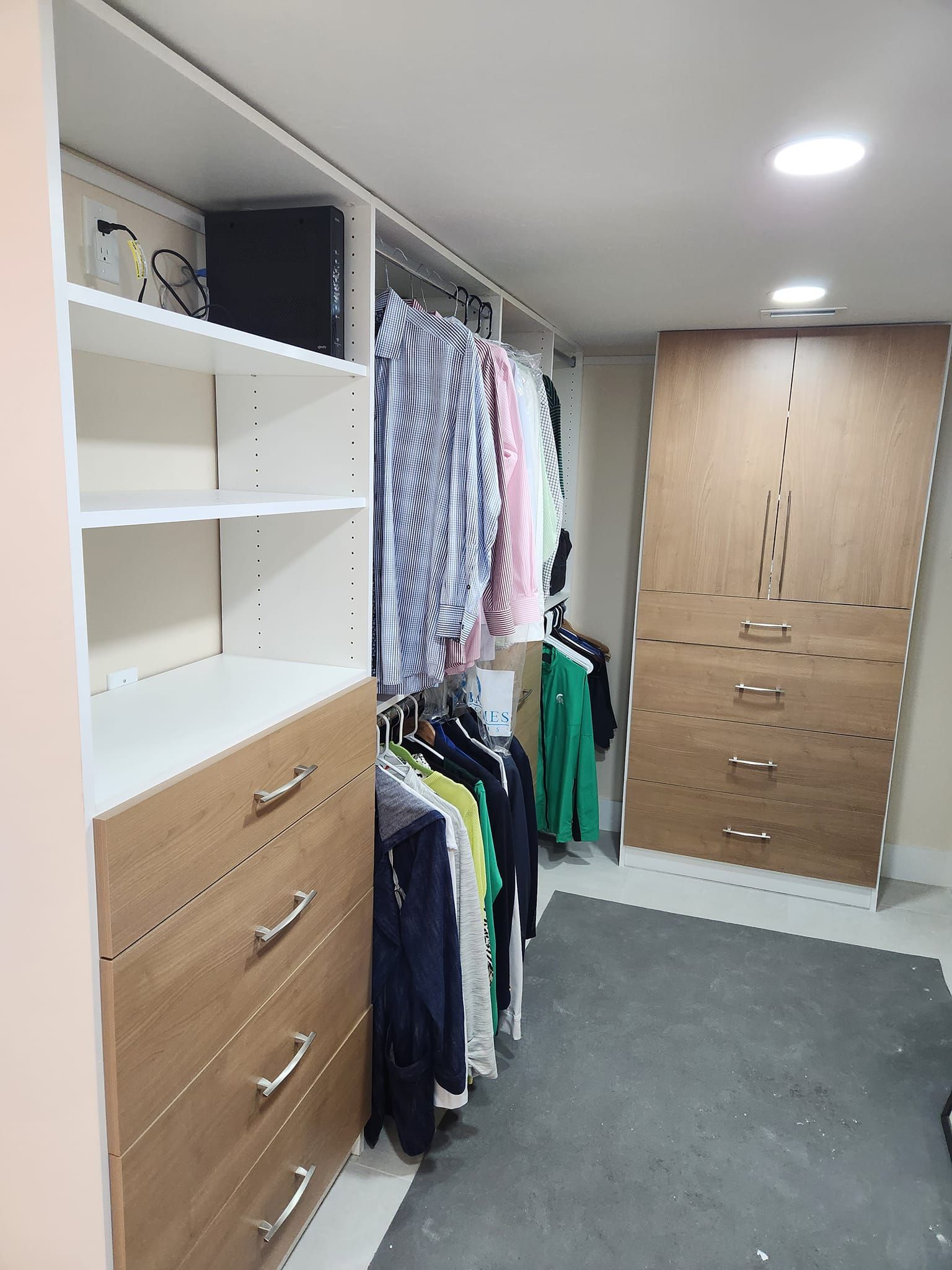 Walk-in closet with shelves, drawers, and hanging clothes. White and wood-toned cabinets.
