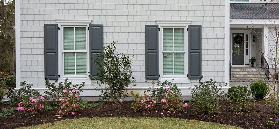 House exterior with gray shutters, white trim, and flowering shrubs.